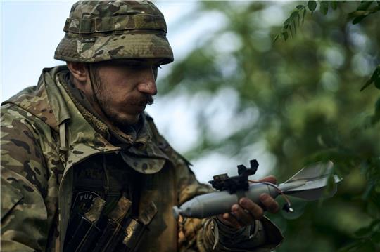 Ein ukrainischer Soldat lädt eine Bombe auf eine Drohne.