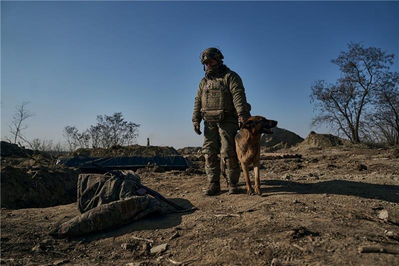 Ein ukrainischer Soldat steht mit seinem Hund an einem Graben in Bachmut.