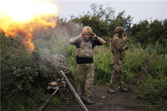 Ein ukrainischer Soldat während eines Funkgesprächs, während ein anderer Soldat 82-mm-Mörser auf russische Stellungen an der Frontlinie in der Nähe Bachmut feuert.
