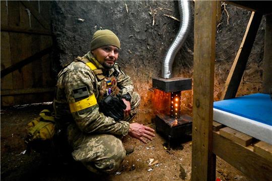 Ein ukrainischer Soldat wärmt sich an einem Ofen.