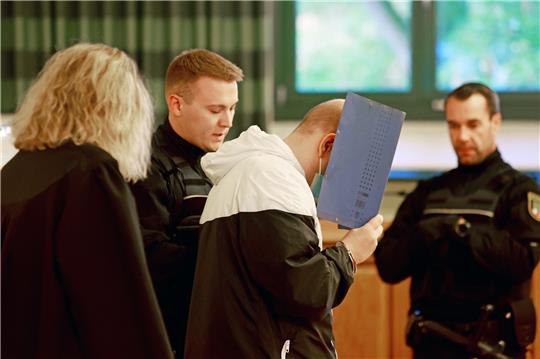 Ein wegen Mordes angeklagter Mann (2.v.r) wird zu Prozessbeginn in den Gerichtssaal gebracht. Foto: picture alliance/dpa | Matthias Bein