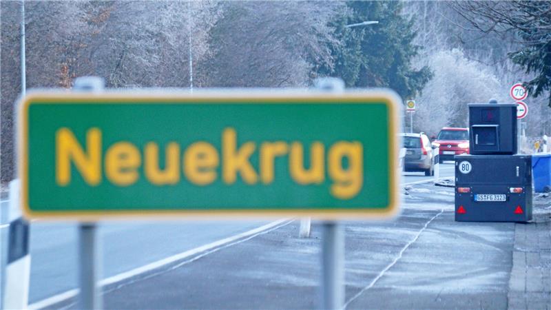 Blitzeranhänger am Straßenrand, im Vordergrund ein Schild, das auf den Ortsteil Neuekrug hinweist.