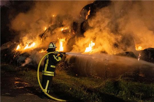 Ein Feuerwehrmann löscht brennende Strohballen.