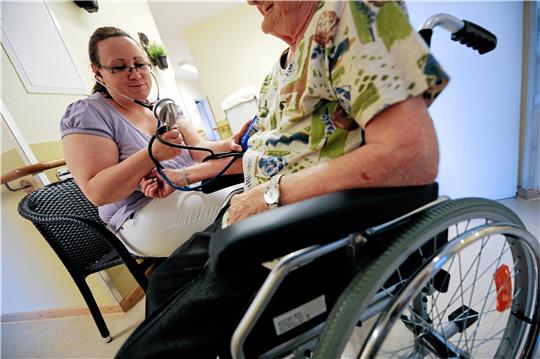 Eine Altenpflegerin hilft einer im Rollstuhl sitzenden Seniorin. Foto: dpa
