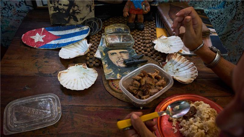 Eine Angestellte eines Souvenirgeschäfts in Havanna isst neben Bildern von Che Guevara, Fidel Castro und Ernest Hemingway.