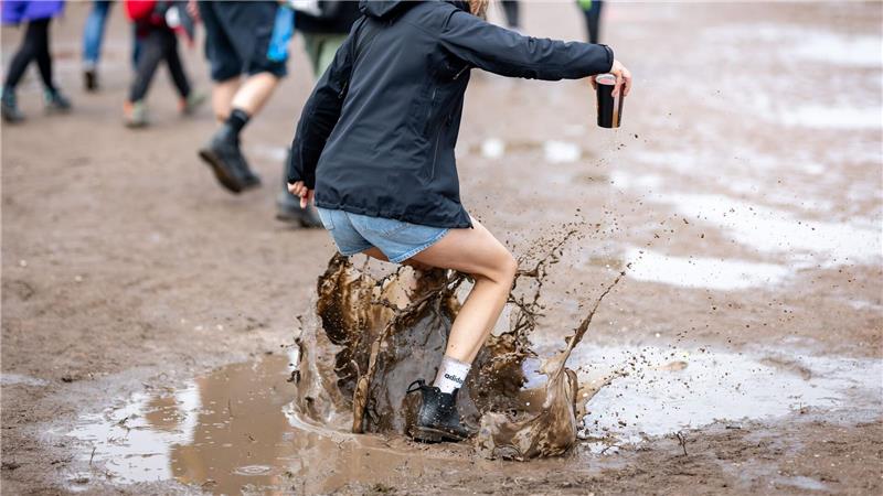 Eine Besucherin des Open-Air-Festivals „Rock im Park“ springt in eine Pfütze.