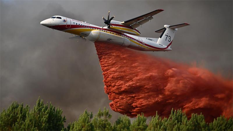 Eine De Havilland Canada Dash 8-400 versprüht Löschmittel, während sie bei den Waldbränden im Südwesten Frankreichs über einen Wald fliegt.