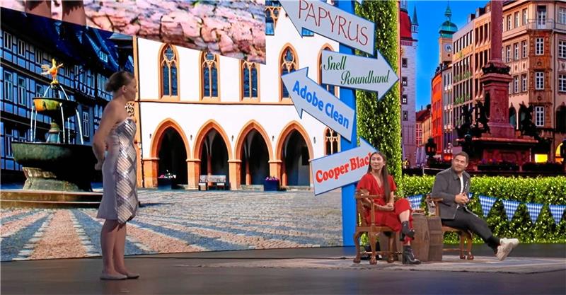 Software-Riese schmückt sich mit Goslarer Welterbe Eine Entwicklerin (links) präsentiert auf der weltweit größten Kreativkonferenz „Adobe Max“ in Los Angeles ein Kleid, das auf Knopfdruck Farbe und Muster wechselt. Im Hintergrund der Bühne ist der Goslarer Marktplatz zu erkennen. Screenshot: Youtube