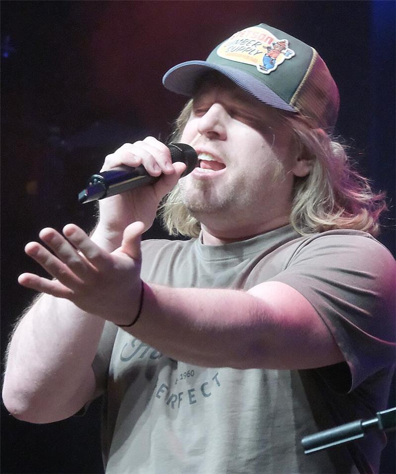 Ein Mann, dessen blonde Locken unter der Schirmmütze herausquellen, singt ins Mikro.