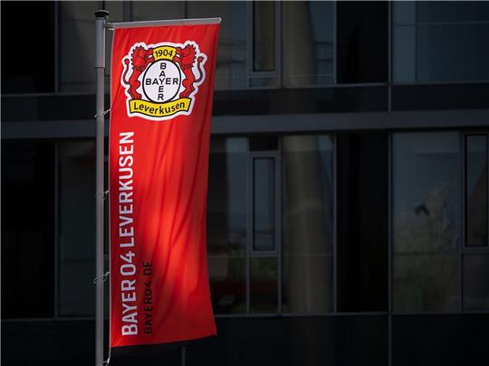 Eine Fahne weht vor der BayArena, dem Stadion des Fußball-Bundesligisten Bayer 04 Leverkusen, und wird dabei von der Sonne angeschienen.