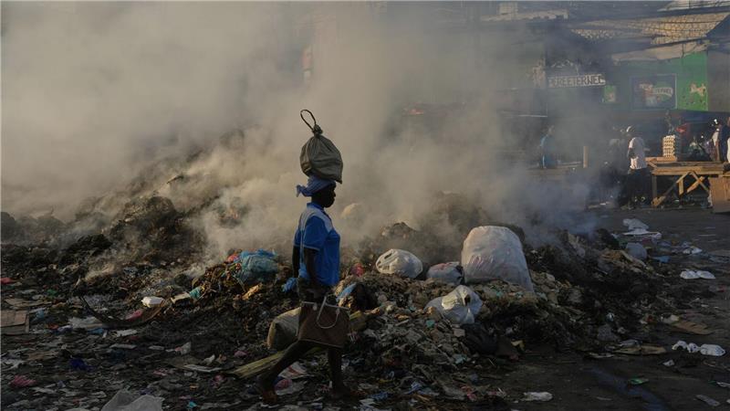 Eine Frau, die eine Tasche auf dem Kopf trägt, geht im Stadtteil Petion-Ville von Port-au-Prince an schwelendem Müll vorbei.