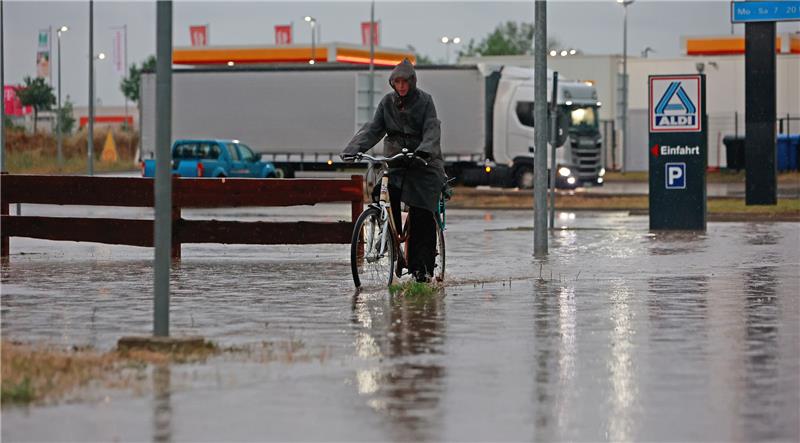 „Lambert“ hält die Region in Atem – Goslar bleibt verschont Eine Frau fährt nach einem Unwetter mit Starkregen mit ihrem Fahrrad über eine überflutete Straße in einem Gewerbegebiet in Blankenburg. Foto: picture alliance/dpa | Matthias Bein