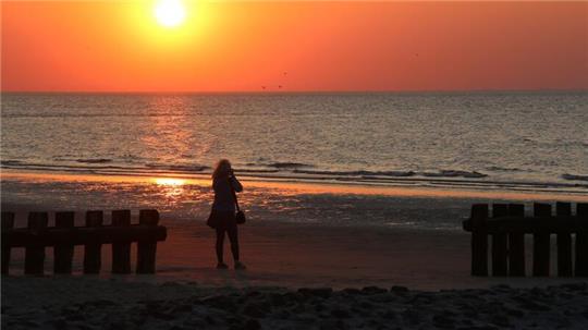 Eine Frau fotografiert am Strand der Insel Wangerooge einen Sonnenuntergang.