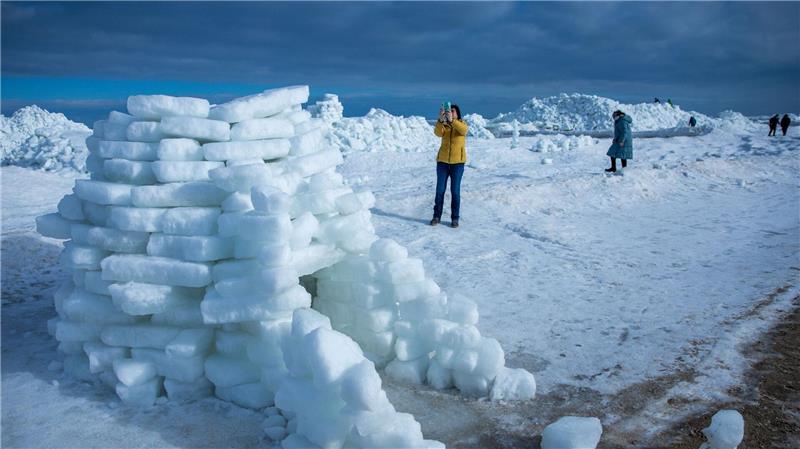 Eine Frau fotografiert ein aus Eisstücken gebautes Iglu vor meterhohen Eisbergen am Ostseestrand auf der Insel Usedom. 