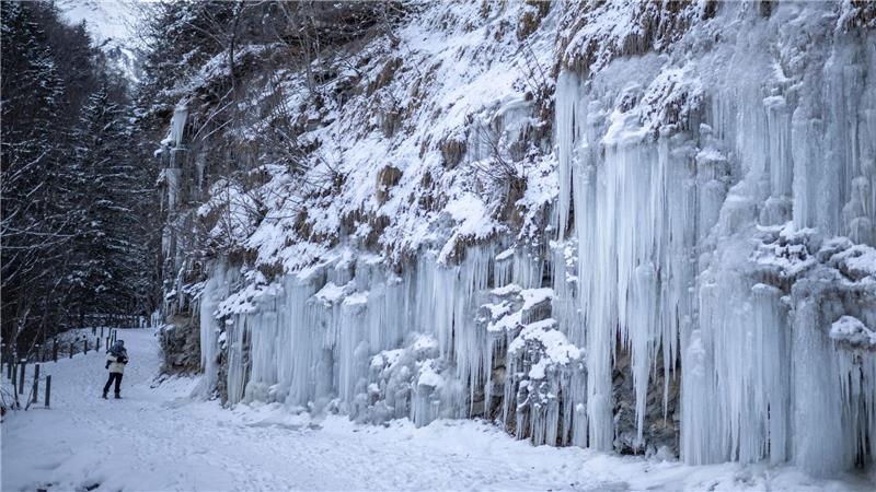 Eine Frau geht mit ihrem Kind auf einem Weg an Eiszapfen vorbei. 