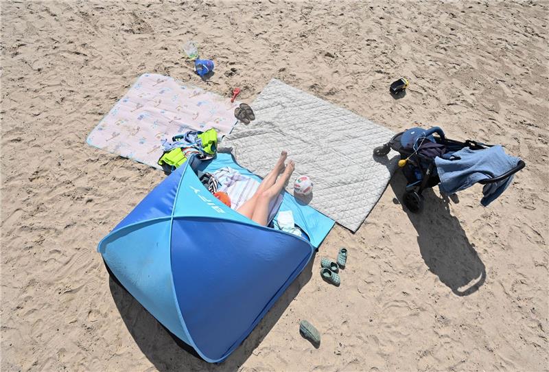 Eine Frau genießt in ihrer Sonnenmuschel das Sommerwetter am Badesee.