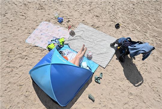 Eine Frau genießt in ihrer Sonnenmuschel das Sommerwetter am Badesee.