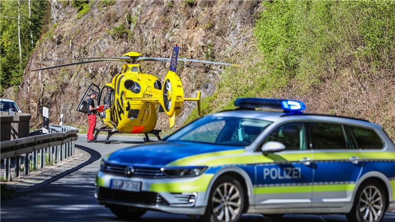 Gelber Rettungshubschrauber auf einer Bergstraße mit einem Polizisten daneben und einem Polizeiauto im Vordergrund