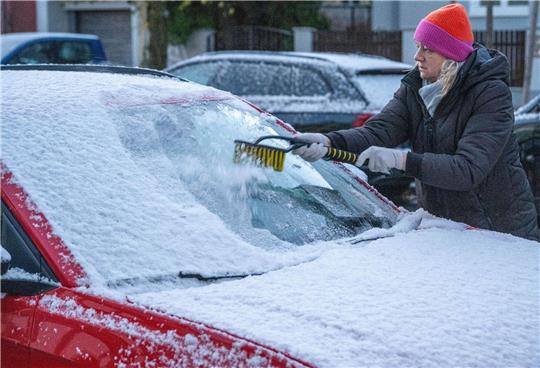 Eine Frau in München befreit am frühen Morgen ein Auto von Schnee und Eis. Auch in den kommenden Tagen soll es winterlich bleiben.