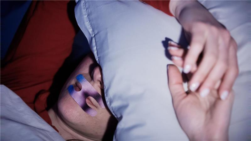 Mouth Taping: Studie warnt vor Risiken von zugeklebtem Mund Eine Frau liegt mit einem Mundpflaster im Bett. Ob es hilft? (Illustration)