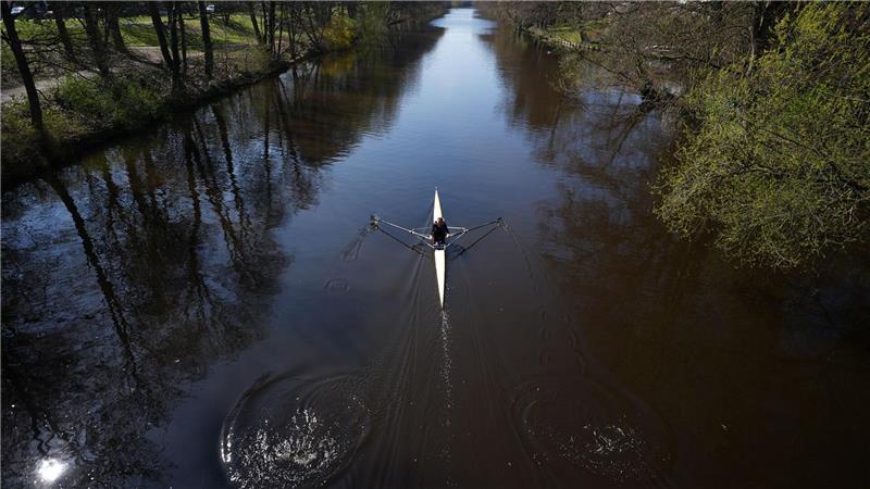 Eine Frau rudert mit ihrem Kajak bei schönstem Sonnenschein auf der Alster in Richtung Außenalster.