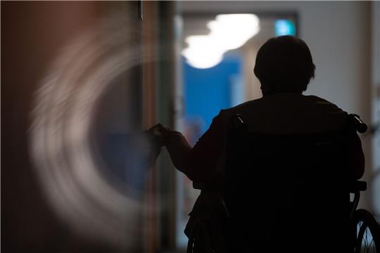 Eine Frau sitzt in einem Alten- und Pflegeheim in einem Rollstuhl auf einem Gang.