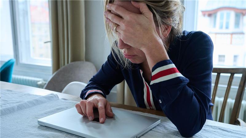 Warum tiefe Seufzer Menschen guttun Eine Frau sitzt vor einem geschlossenen Laptop und seufzt.