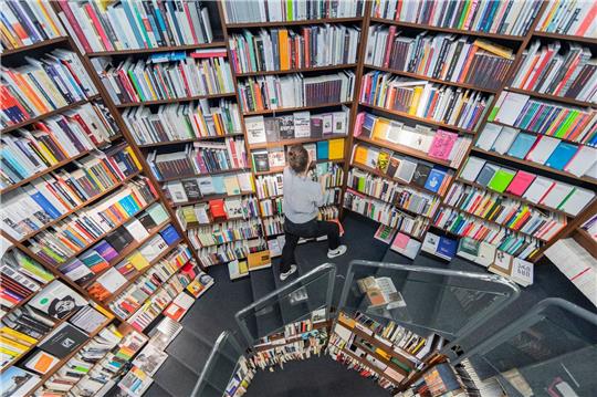 Eine Frau sortiert Bücher in die Regale einer Buchhandlung ein.