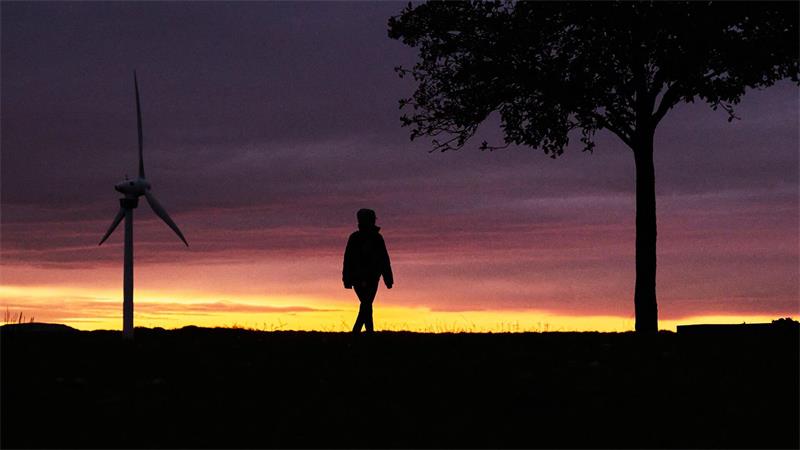 Eine Frau spaziert vor der vom Sonnenaufgang verfärbten morgendlichen Wolkenkulisse bei Hannover. 