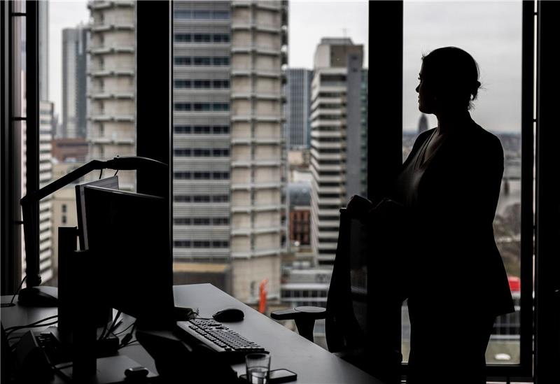 Eine Frau steht an ihrem Arbeitsplatz in einem Hochhaus am Fenster.