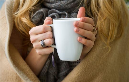 Eine Frau wärmt sich in Hannover, in eine Decke gehüllt, an einer Tasse Tee. Ab wann jemand friert, hängt von vielen Faktoren ab.