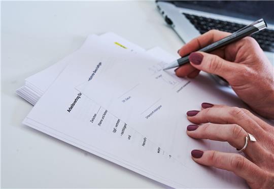 Eine Frauenhand unterschreibt einen Arbeitsvertrag.