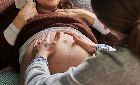 Eine Hebamme tastet in ihrer Berliner Praxis den Bauch einer schwangeren Frau ab.