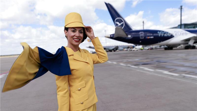 Eine Hostess trägt eine frühere Lufthansa-Uniform vor einem Passagierflugzeug der Lufthansa auf dem Flughafen Berlin-Brandenburg (BER) bei der Feier von Lufthansa zum 100. Jahrestag des Erstflugs.