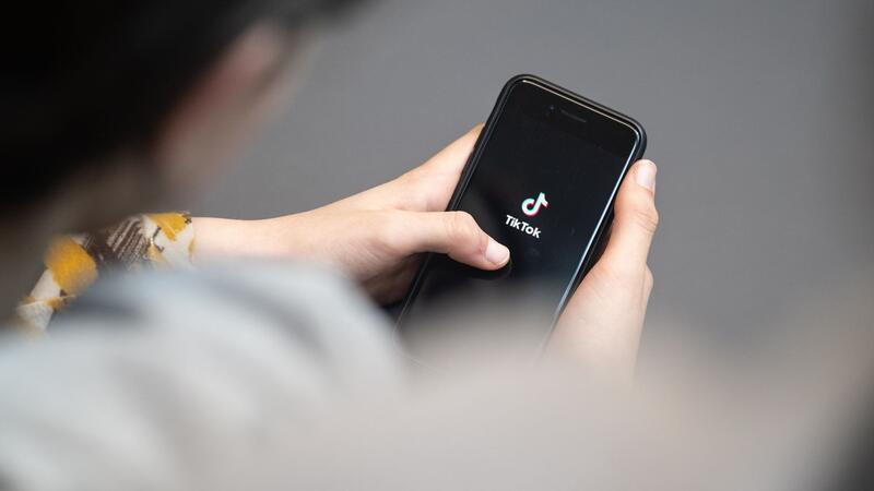 Eine Jugendliche schaut auf ein Smartphone mit angezeigtem TikTok Logo.