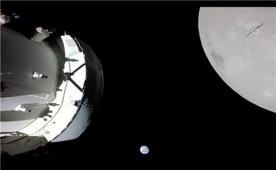 Eine Kamera an Bord der «Orion»-Kapsel zeigt das Raumschiff (l) im Weltraum, den Mond (r) und klein im Hintergrund die Erde.