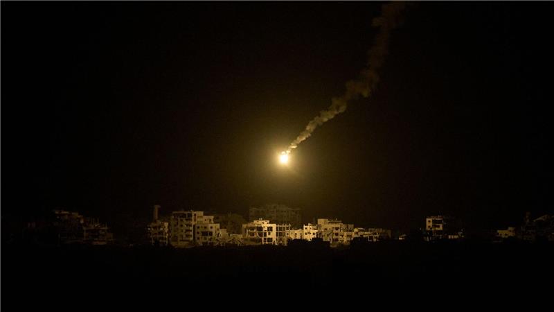 Eine Leuchtrakete der israelischen Armee fliegt über Gebäuden, die während der israelischen Boden- und Luftoperationen im nördlichen Gazastreifen zerstört wurden.