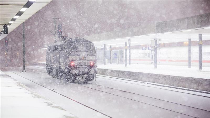 Eine Lok steht am frühen Morgen an einem verschneiten Gleis im Hauptbahnhof Hannover. 
