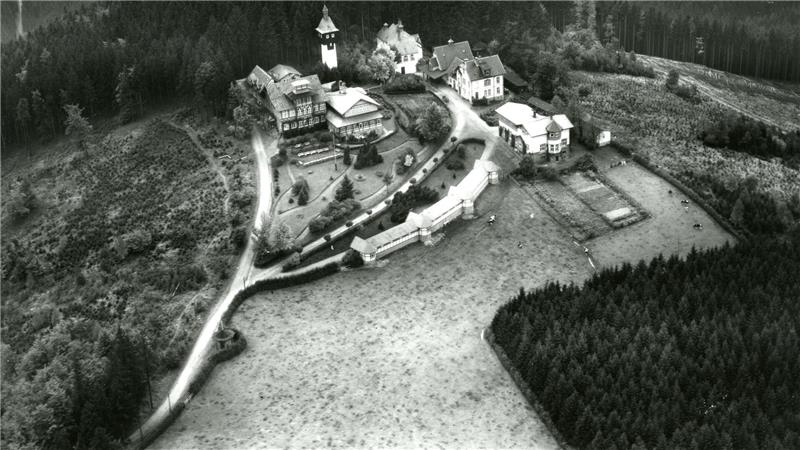 Luftaufnahme eines abgelegenen Bergdorfes mit mehreren Gebäuden, umgeben von Wald und Wiesen