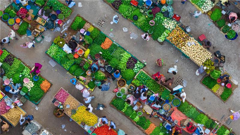 Eine Luftaufnahme zeigt das lebhafte Treiben auf einem Gemüsemarkt in Ahmedabad in Indien, wo Verkäufer frische Produkte anordnen und Kunden sich durch die engen Marktgassen bewegen.
