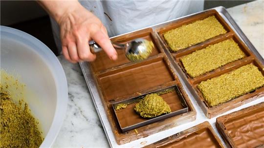 Eine Mitarbeiterin der Manufatur Trüffel Güse befüllt bei der Herstellung von Dubai-Schokolade die Schokoladentafeln mit einer Creme aus Pistazienmus und Engelshaar. Der Hype rund um die Dubai-Schokoladen ist ungebrochen.