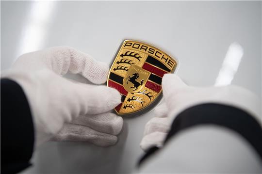 Eine Mitarbeiterin der Porsche AG hält in der Produktion ein Porsche-Emblem.