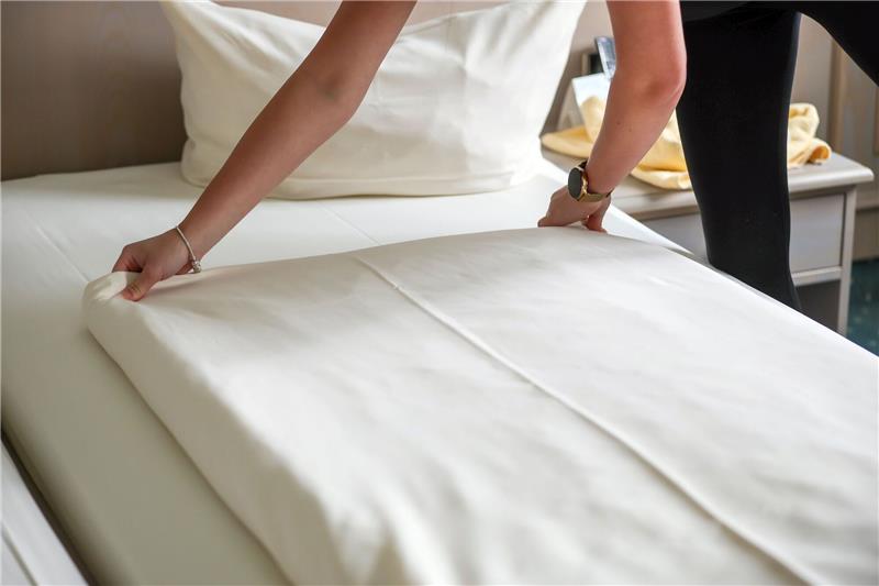 Eine Mitarbeiterin eines Hotels streicht eine Bettdecke in einem Hotelzimmer glatt.