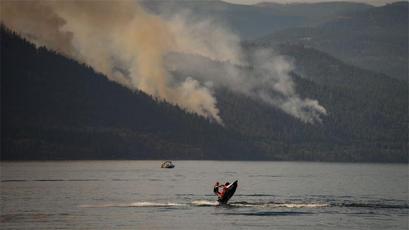 Eine Person fährt mit einem Jetski in Kanada, währen im Hintergrund ein Wald brennt.
