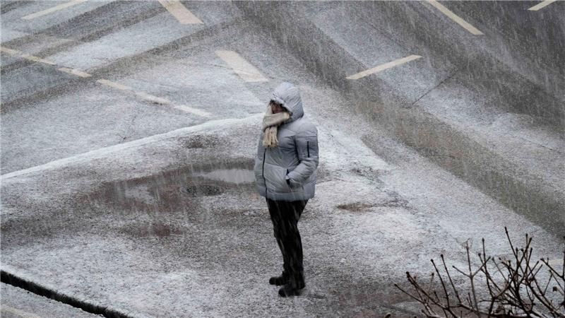 Eine Person steht bei starkem Schneefall an einer Kreuzung in Frankfurt. 