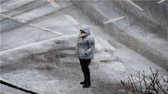 Eine Person steht bei starkem Schneefall an einer Kreuzung in Frankfurt. 