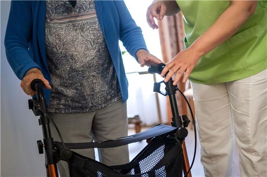 Eine Pflegefachkraft hilft einer Bewohnerin in einem Seniorenheim mit ihrem Rollator.