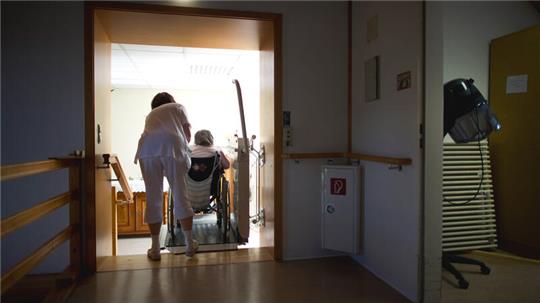 Eine Pflegerin hilft der Bewohnerin eines Altenpflegeheimes mit einer Rollstuhlhilfe eine Treppe hinauf: Der Landkreis Goslar trägt für viele Menschen einen Teil der Kosten für ihren Heimaufenthalt. Das ist einer der Gründe für die aktuell steigenden Sozialausgaben.
