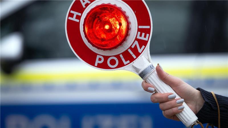 Eine Polizistin hält während einer Verkehrskontrolle eine Polizeikelle mit der Aufschrift „Halt Polizei“.