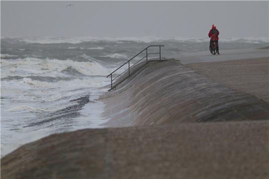 Eine Radfahrerin steht bei stürmischem Wetter an der Wasserkante auf der Insel Norderney. Ein Tiefausläufer sorgt für stürmisches Wetter im Norden.